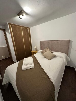 A hotel room with a bed, a nightstand, a lamp, and a wooden wardrobe.