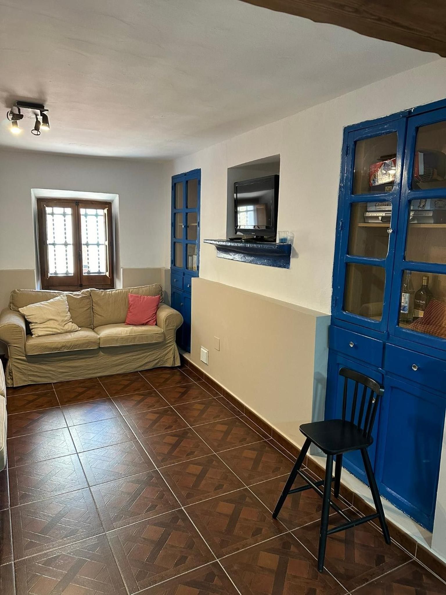Una sala de estar con un sofá, un televisor montado en la pared y un mueble azul con puertas de cristal.