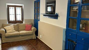 Una sala de estar con un sofá, un televisor montado en la pared y un mueble azul con puertas de cristal.