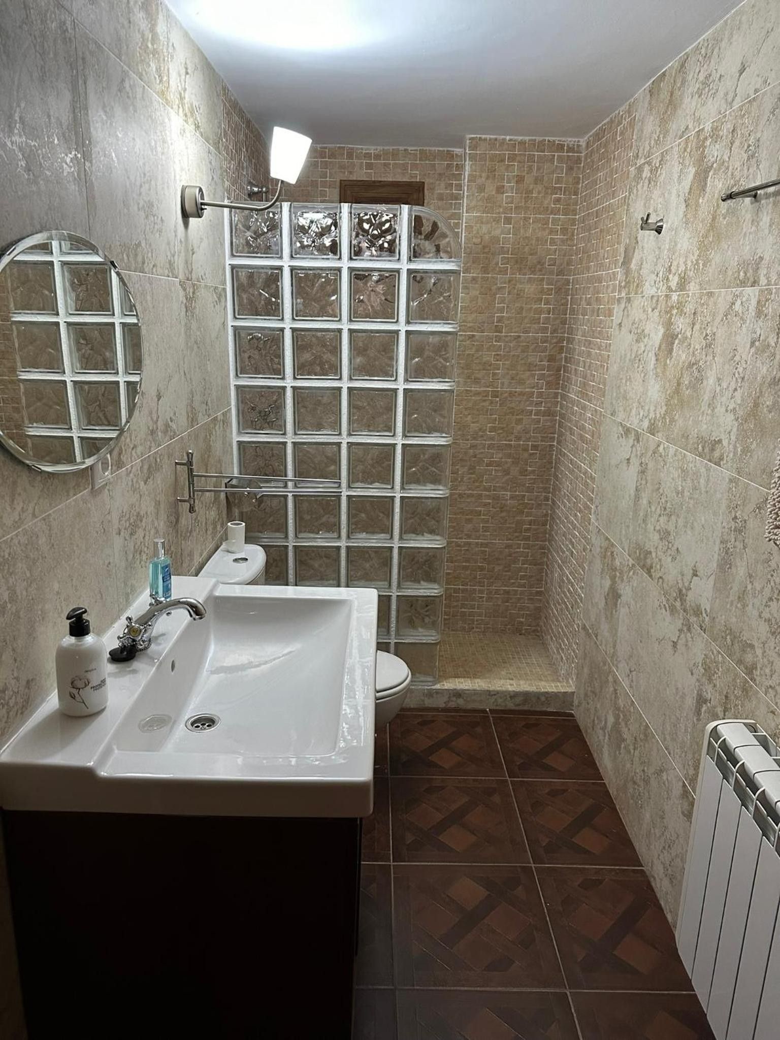 Un baño con un lavabo blanco, un espejo, ducha con puerta de cristal y un inodoro.