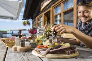 A wooden table with a variety of food items, including sliced meats and vegetables, and a bottle of oil. - Haus Thon holiday apartment garden view (Bodensdorf)