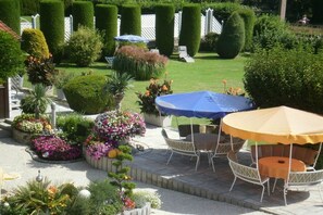 A garden patio with a table and chairs, surrounded by neatly trimmed hedges and flower beds. - Haus Thon holiday apartment garden view (Bodensdorf)