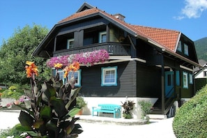 A two-story house with a balcony, a bench, and a garden with flowers. - Haus Thon holiday apartment garden view (Bodensdorf)