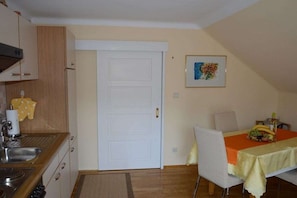 A compact kitchen with a white door, a dining area with a table set for two, and a small window. - Haus Thon holiday apartment garden view (Bodensdorf)