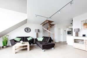 A modern living room with a black leather sofa, a wooden coffee table, and a staircase leading to an upper level. - Holiday apartment in Norderney with sauna (Norderney)