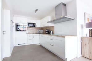 A modern kitchen with white cabinetry, a microwave, a stove, and a coffee maker. - Holiday apartment in Norderney with sauna (Norderney)