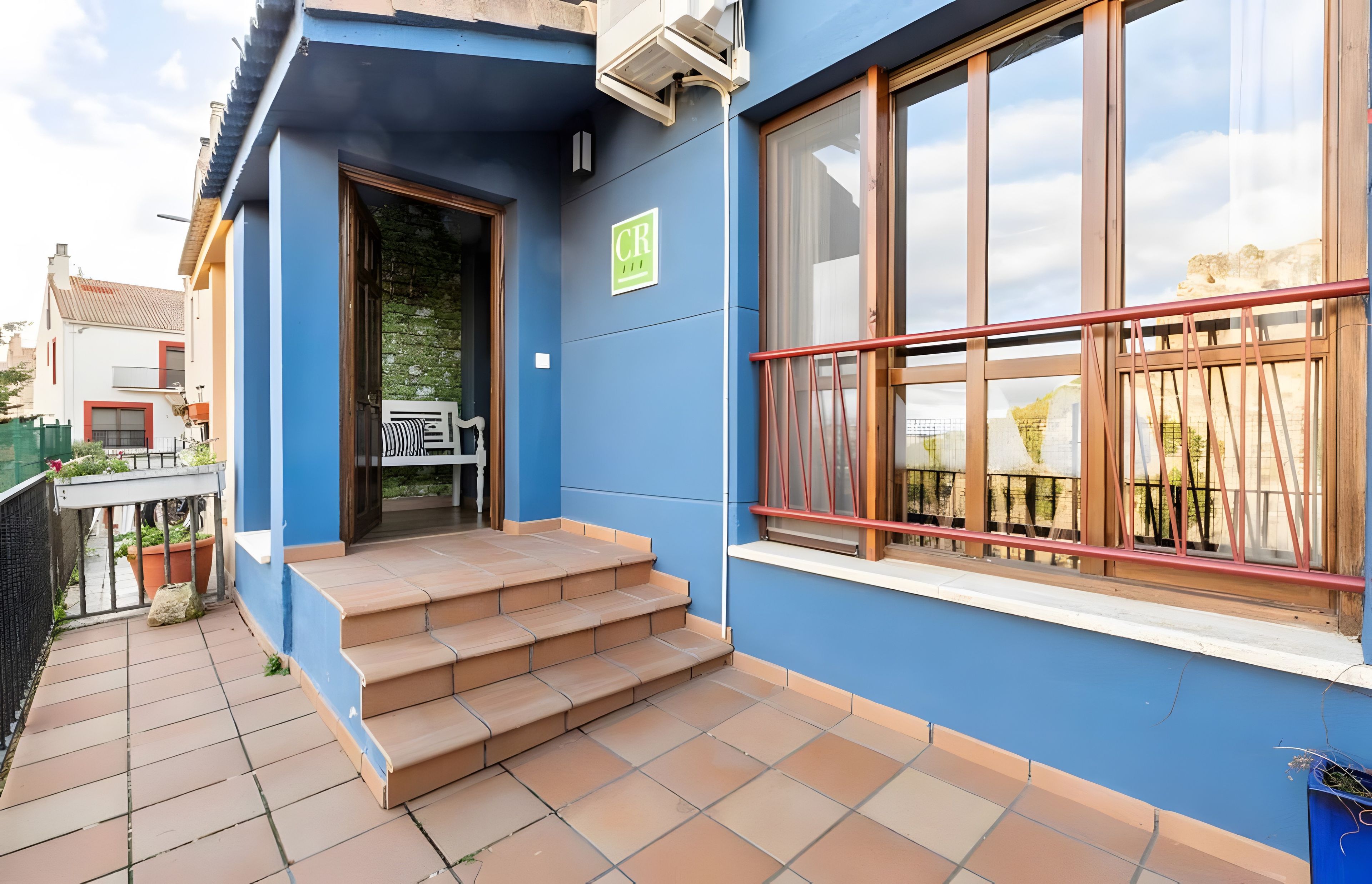Un edificio azul con una escalera que lleva a una puerta, una ventana con marco rojo y un letrero verde con las letras 'CR'.