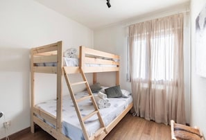 Una cama litera con escalera, una cama individual y una silla en una habitación con ventana y cortinas.