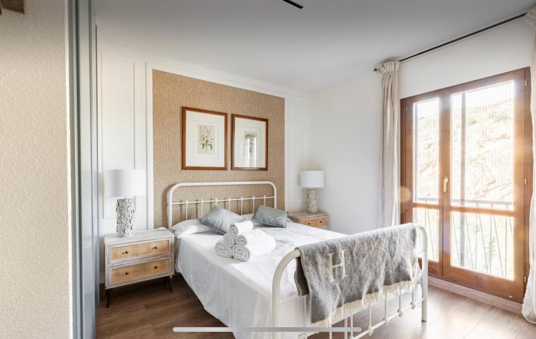 Ein Schlafzimmer mit einem Bett, Nachttischen, einem Fenster mit Vorhängen und Wandbildern.
