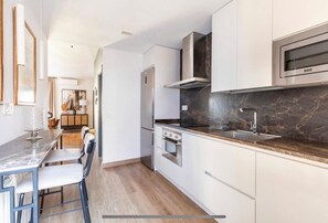 Cocina moderna con armarios blancos, un refrigerador de acero inoxidable, horno empotrado y microondas.