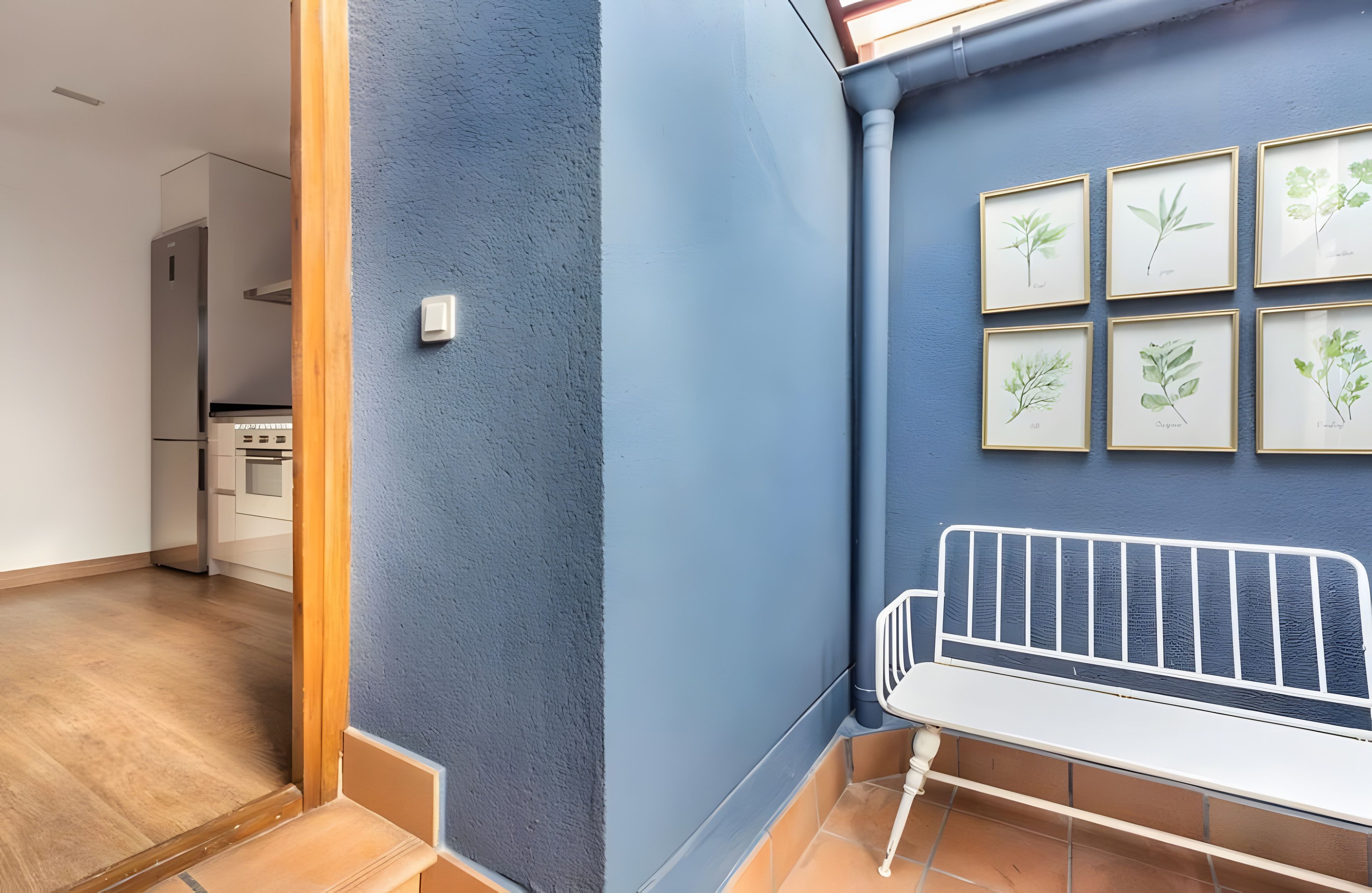 Ein Flur mit blauer Wand, einer weißen Bank und gerahmten Pflanzenbildern.