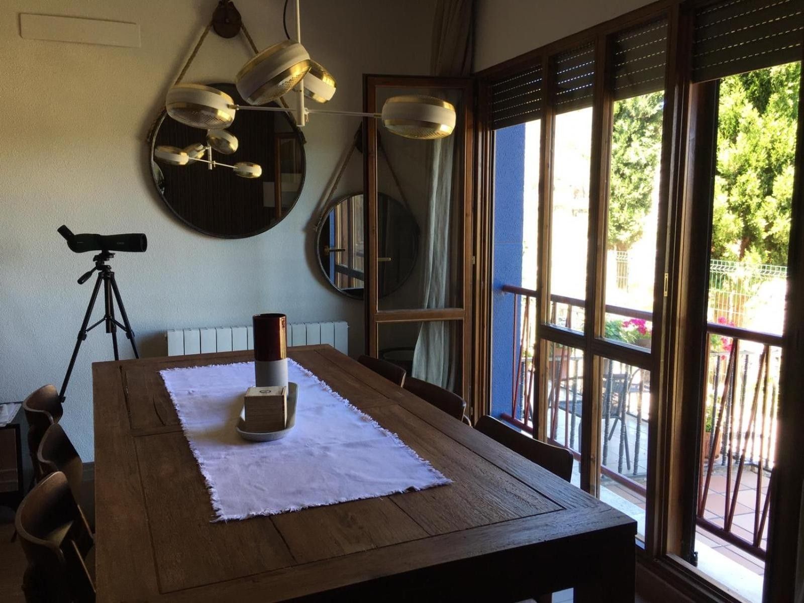 Un comedor con una mesa de madera, un telescopio y ventanas amplias con vistas a la vegetación.