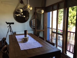 Un comedor con una mesa de madera, un telescopio y ventanas amplias con vistas a la vegetación.