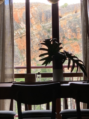 Un comedor con una mesa y sillas, una planta en maceta y vistas a un paisaje rocoso a través de amplios ventanales.