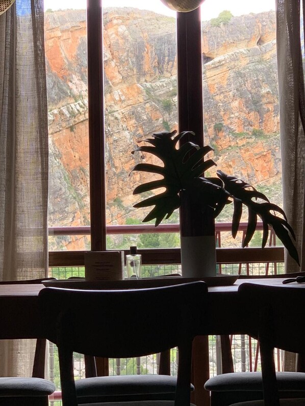 Un comedor con una mesa y sillas, una planta en maceta y vistas a un paisaje rocoso a través de amplios ventanales.
