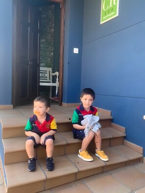 Two children sitting on outdoor steps with a building entrance in the background.