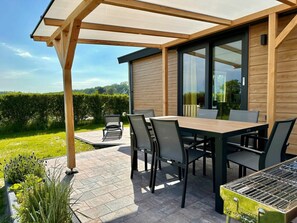 An outdoor patio with a wooden table and chairs, a grill, and a view of a green landscape. - Puik en Duin 5a (Noordwijk)
