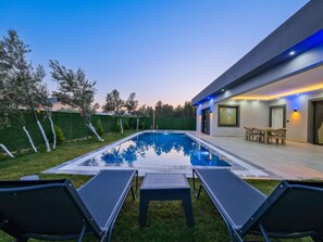 A modern outdoor pool area with lounge chairs, a dining table, and a well-maintained lawn. - Villa in Fethiye/mugla With Swimming Pool (Fethiye)