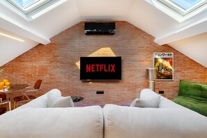 Ein modernes Wohnzimmer mit Backsteinwand, einem Wand-Fernseher und einem grünen Sofa.