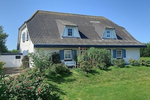 Ein zweistöckiges Haus mit Satteldach, einer Veranda und einem kleinen Garten.