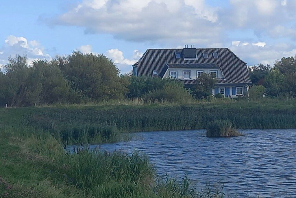 Ein Haus mit geneigtem Dach, eingebettet in eine natürliche Landschaft mit einem Gewässer im Vordergrund.