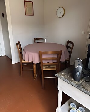 Ein Essbereich mit einem runden Tisch, vier Stühlen, einer Wanduhr und einer Kaffeemaschine auf dem Tisch.