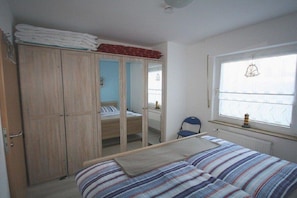 Une chambre à coucher avec un lit, une armoire, un miroir et une fenêtre donnant sur un beau paysage.