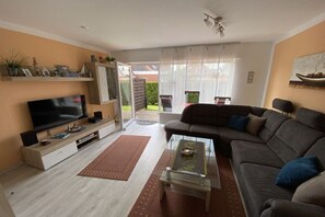 A living room with a flat-screen TV, a sofa, a coffee table, and a sliding glass door leading to an outdoor area. - Holiday apartment with 1 bedroom (Norden)