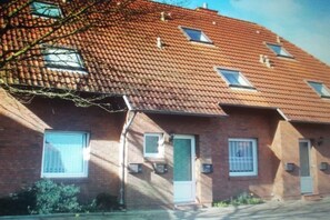 A two-story brick building with a red-tiled roof, multiple windows, and a visible door. - Holiday apartment with 1 bedroom (Norden)