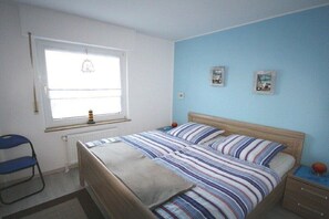 A bedroom with a double bed, a window with a curtain, a radiator, and two framed pictures on the wall. - Holiday apartment with 1 bedroom (Norden)