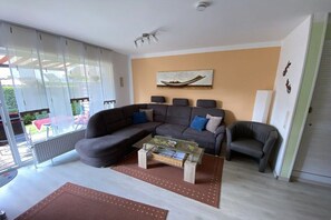 A modern living room with a sectional sofa, a glass coffee table, and a view through large sliding glass doors. - Holiday apartment with 1 bedroom (Norden)