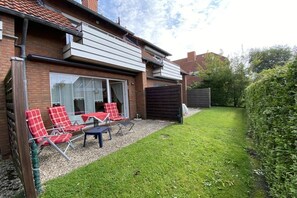 A residential property with a patio area, outdoor seating, and a well-maintained lawn. - Holiday apartment with 1 bedroom (Norden)