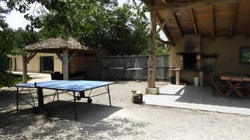 Un patio al aire libre con mesa de ping pong, zona de estar cubierta y una parrilla.
