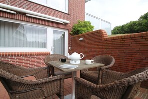 A patio with wicker chairs, a table, and a white teapot. - "Tied" at Uns to Hus (Juist)