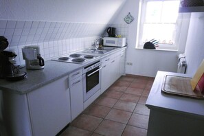 A compact kitchen with white cabinets, a stove, a microwave, and a window. - Holiday apartment with 2 bedrooms (Hooksiel)