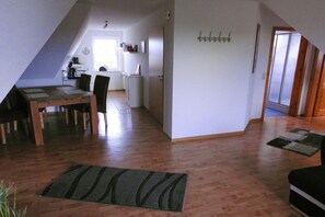 A spacious living area with a dining table and chairs, a kitchen in the background, and a door leading to another room. - Holiday apartment with 2 bedrooms (Hooksiel)