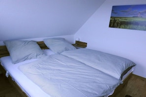 Een enkel bed met een witte matras en twee kussens, een houten hoofdbord en een aan de muur hangend landschapsbeeld.
