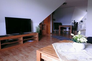 A living room with a television on a wooden stand, a dining area with a table and chairs, and a kitchen in the background. - Holiday apartment with 2 bedrooms (Hooksiel)