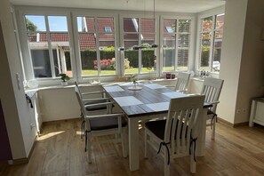 A dining area with a large table and chairs, a window with a view of a garden, and a pendant light. - Holiday home in Langeoog with swimming pool (Langeoog)