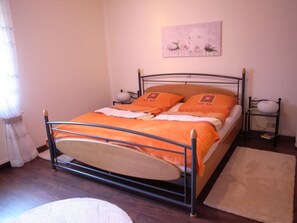 Ein Einzelbett mit orangefarbener Bettdecke und Kissen, ein Nachttisch mit Lampe sowie ein Bild an der Wand.