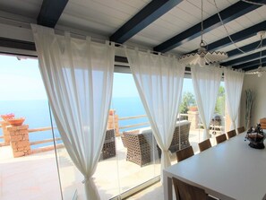 A room with a large window, white curtains, a table, and a view of the sea. - 3-bedroom Villa (Trinità d'Agultu e Vignola)
