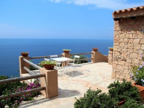 A terrace with a stone wall, a table, chairs, and potted plants overlooking the sea. - 3-bedroom Villa (Trinità d'Agultu e Vignola)