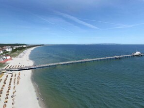 Ein Küstenstrand mit einer langen Pier, die sich ins Meer erstreckt, einem sandigen Ufer und einem klaren Himmel.