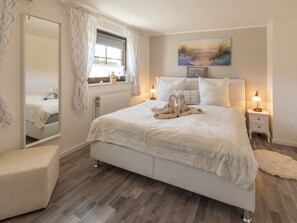 A bedroom with a large bed, bedside lamps, a window with curtains, a mirror, and a painting on the wall. - Holiday Apartment With 1 Bedroom (Sellin)