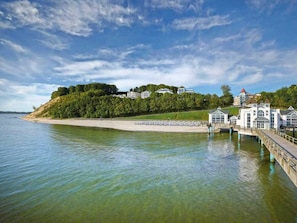 A coastal hotel with a beach, a pier, and a forested hill in the background. - Holiday Apartment With 1 Bedroom (Sellin)