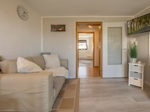A living room with a beige sofa, a clock on the wall, and a door leading to a bathroom. - Holiday Apartment With 1 Bedroom (Sellin)