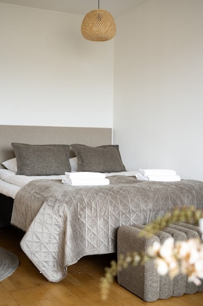 Een net opgemaakt bed met een grijze deken, twee kussens en een opgevouwen witte handdoek.