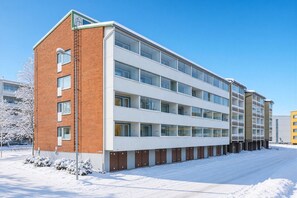 Ein mehrstöckiges Gebäude mit Backsteinfassade und großen Fenstern, mit einem flachen Dach und einem mit Schnee bedeckten Untergrund.