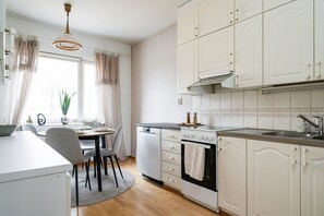 A modern kitchen with white cabinetry, a dining area with a round table, and a window with curtains. - Top Floor Park View Home By Lapland Host (Rovaniemi)