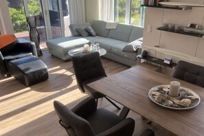 A modern living room with a sofa, chairs, a dining table, and a view through large windows. - Holiday apartment with 2 bedrooms (Wangerooge)